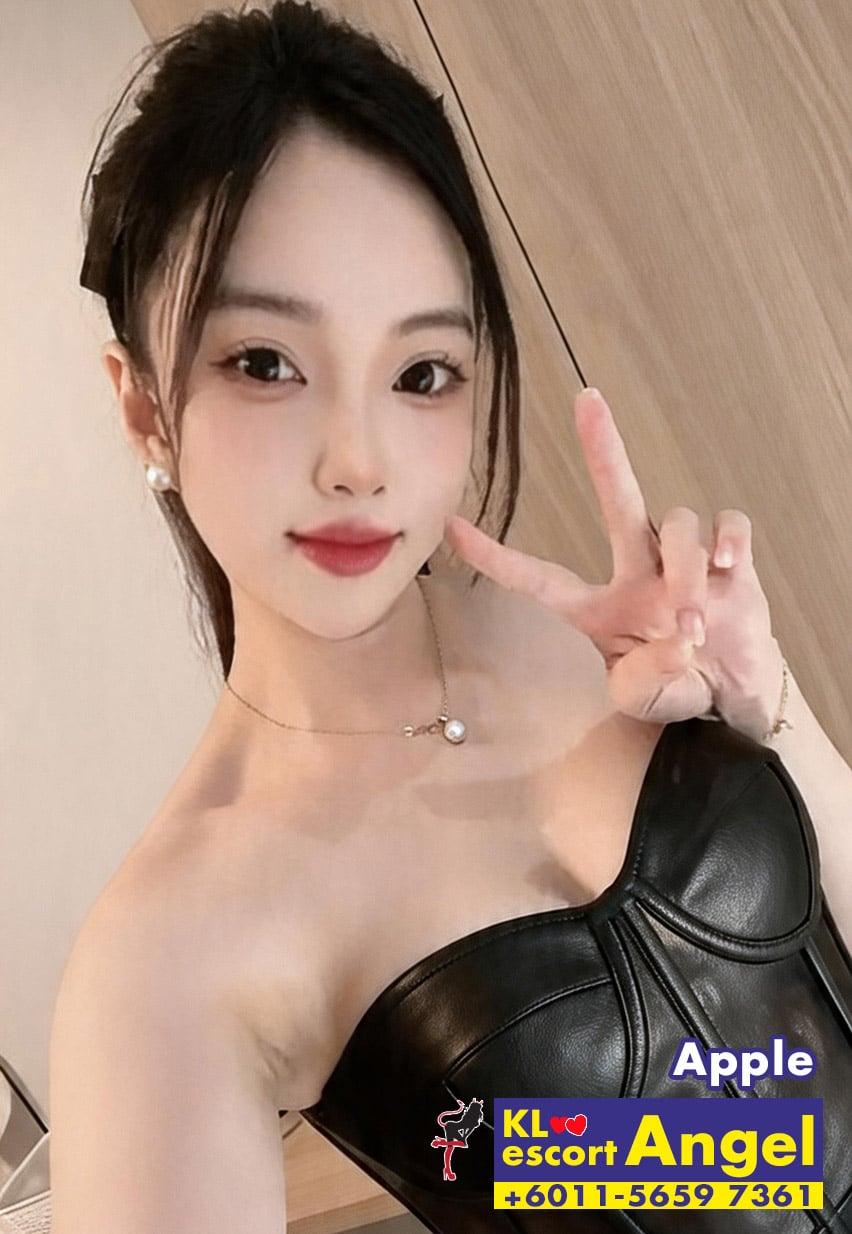 Selfie of a young woman making a peace sign, wearing a black strapless top and a pearl necklace, with an escort ad badge in the corner.