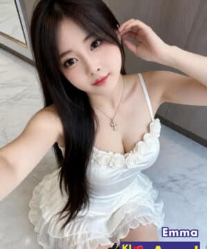 Woman taking a selfie in a white dress with rose trim, long dark hair, and a cross necklace; overlay text reads "Emma" and an escort ad banner with a phone number.